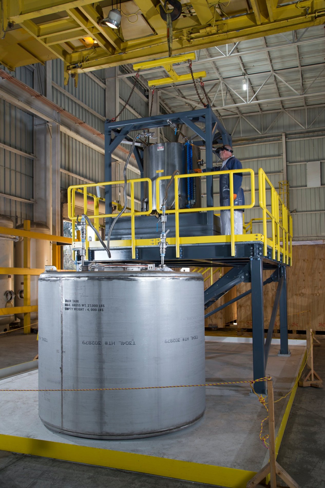 Operator in protective gear working at a guarded platform above a large process tank