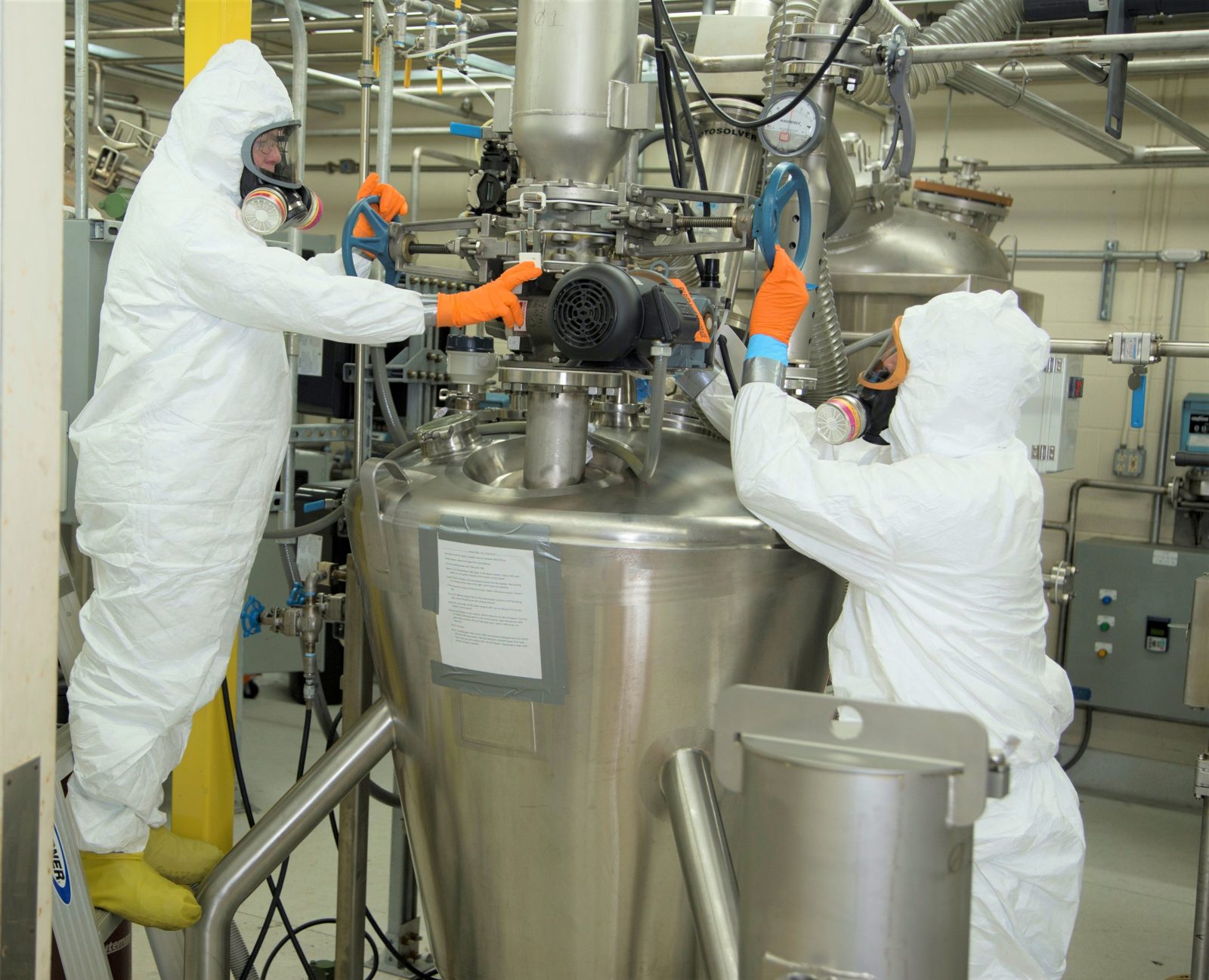 Technicians in protective equipment operating a process vessel